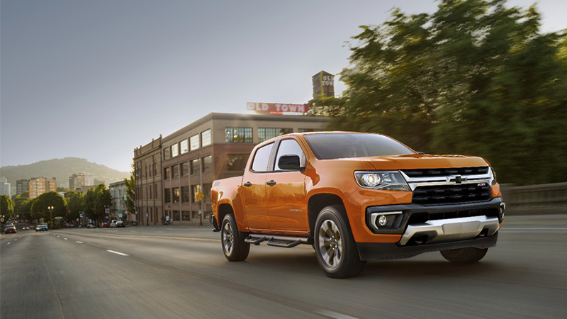 Orange 2021 Chevrolet Colorado driving down a city street. 