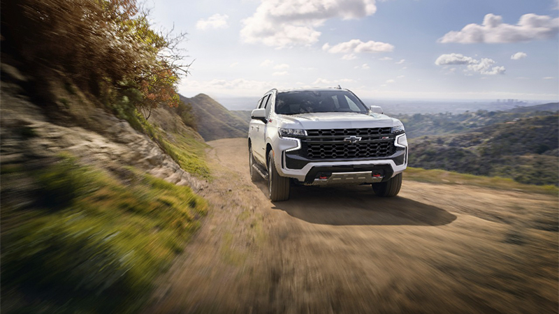 front view of a white Tahoe driving on a dirt mountain road
