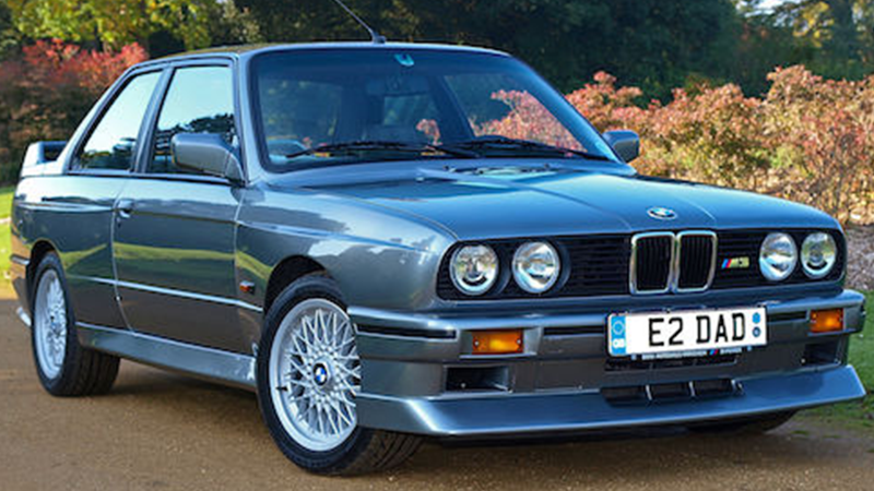 A vintage, dusty blue BMW parked on a curb.