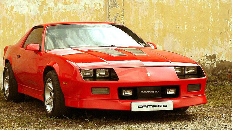 A Red Gen 3 Camaro sits in front of a yellow wall.