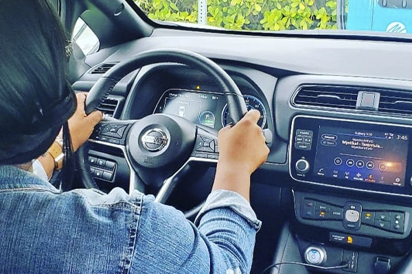 A woman sits with two hands on the wheel of a car