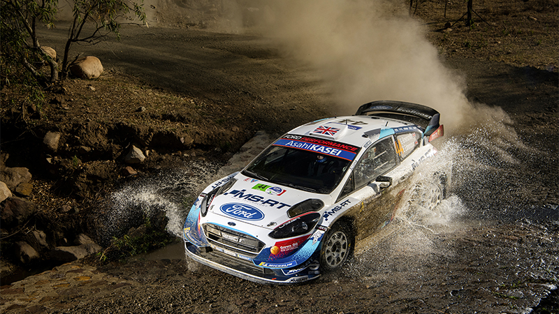 Gus Greensmith in a rally car on track with a dust trail behind