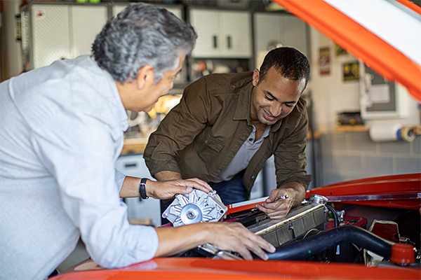 two men look under the hood of a red car
