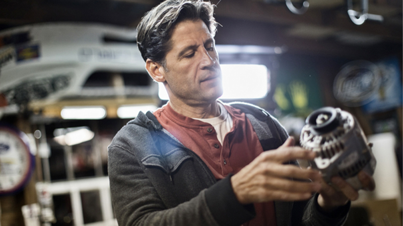 a man in a home garage looks at an alternator he's holding