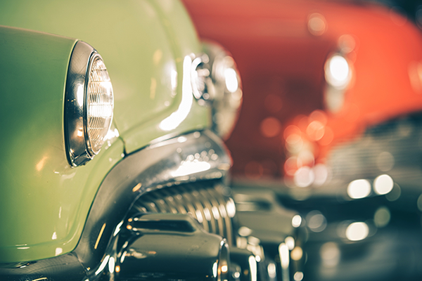 A green vintage car sits at an auction next to a red one