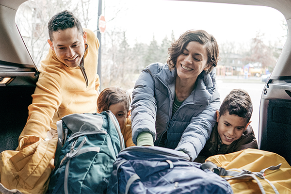 a family with two children places bags in the back of an SUV