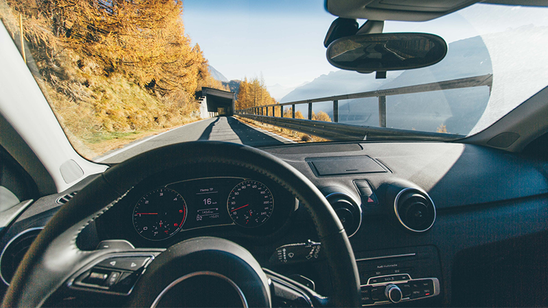 a view from the driver's seat looking past the steering wheel at a mountain landscape around the road
