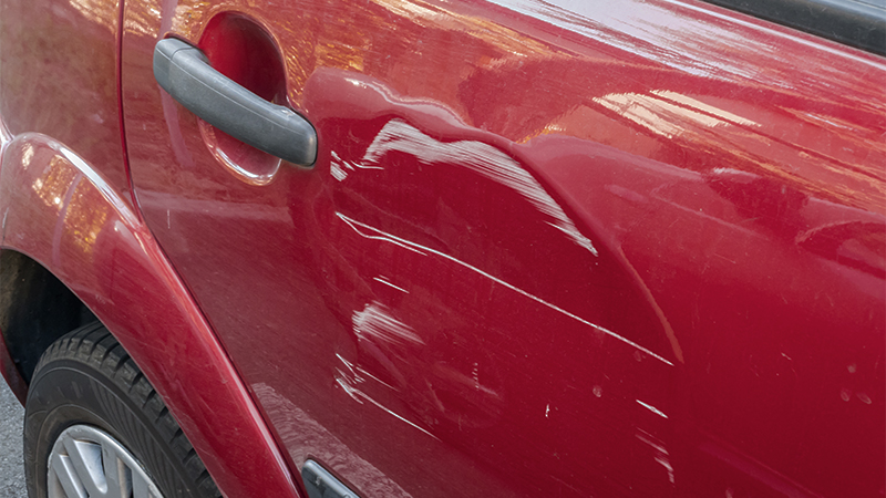 a dent and white scratched paint on the rear passenger side door of a red vehicle