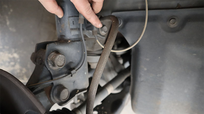 a hand points to a bolt securing a brake line bracket to the strut