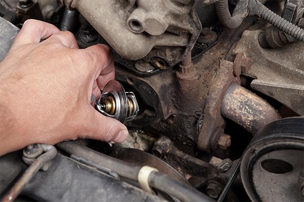 A closeup view of a new thermostat being placed in the housing of an engine