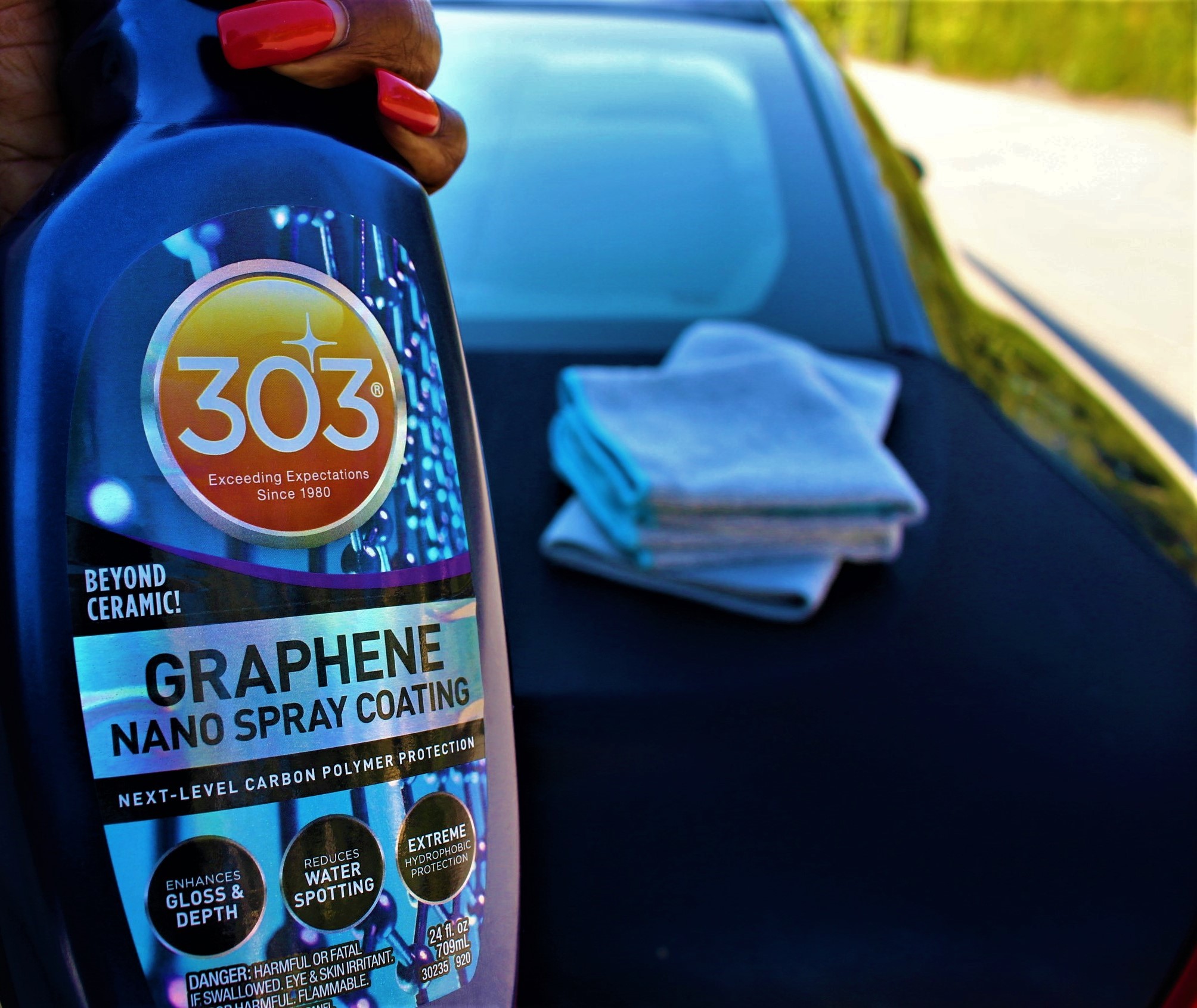 closeup of a 303 Graphene Nano Spray bottle held by a woman's hand with bright red nails