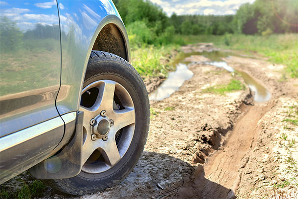 a side view of a car with a long, muddy road ahead